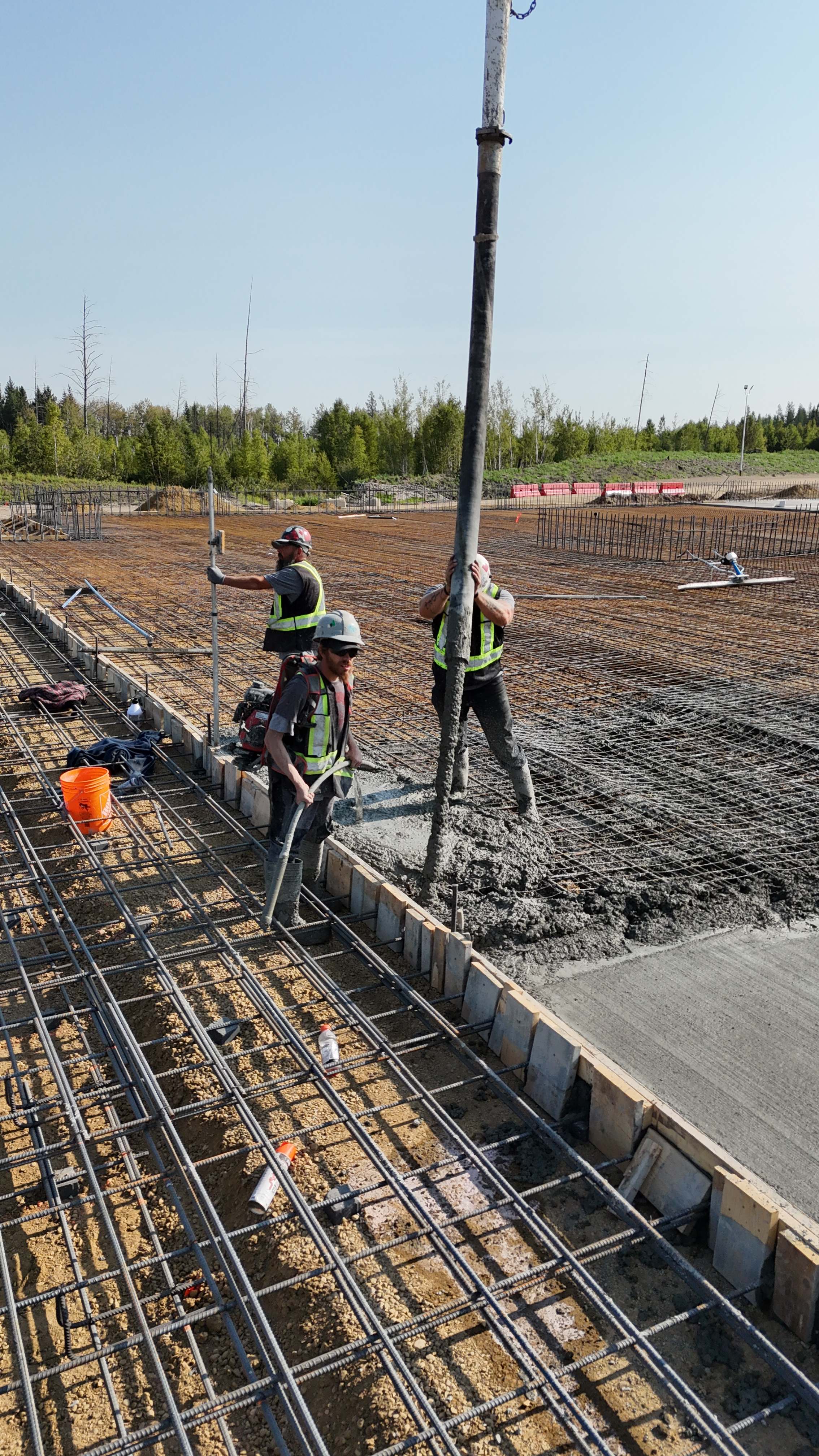 Workers pouring concrete with rebar installation on outdoor construction site