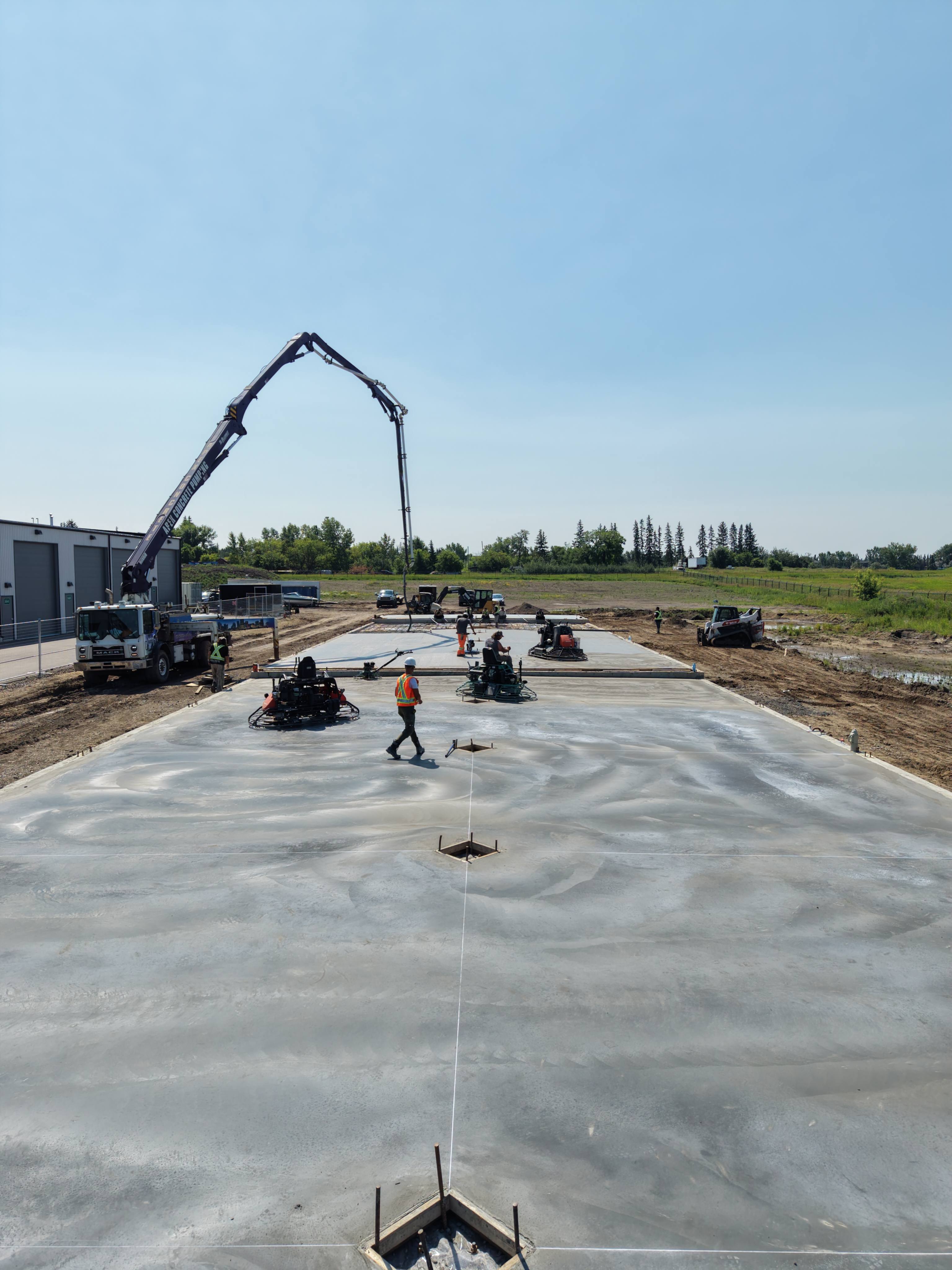 Drone aerial view of Fullcrete crew finishing large concrete slab with boom pump truck and ride-on trowels